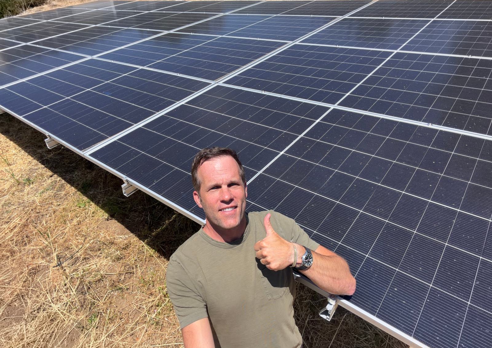 Scott Mueller, founder, giving a thumbs up beside a large ground-mounted solar array